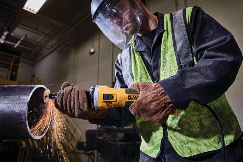 A person wearing safety gear uses a DEWALT power tool to grind or cut a metal pipe, producing sparks.