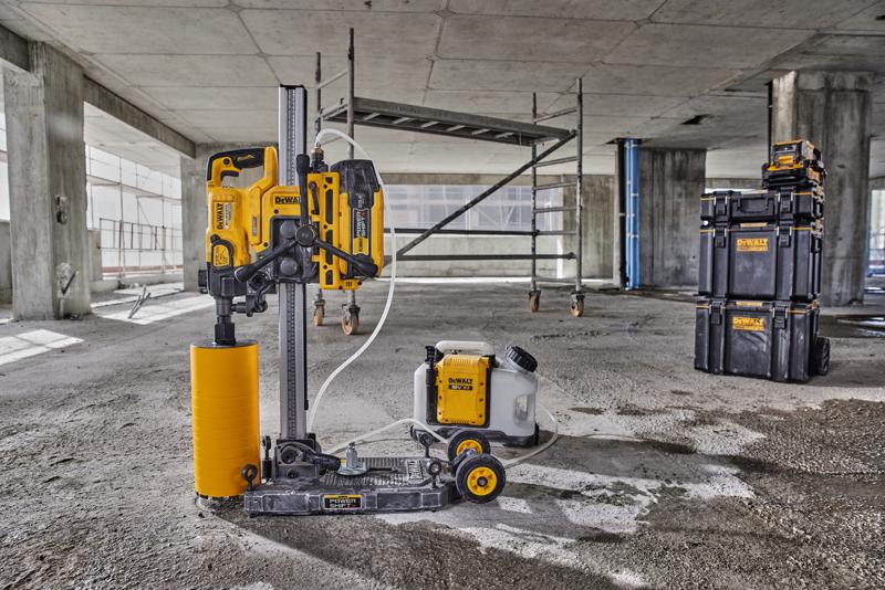 DEWALT DCPS151 core drilling machine with yellow and black design, water tank, and accessories, set up on a concrete floor in a construction site with scaffold and DEWALT storage boxes in the background.