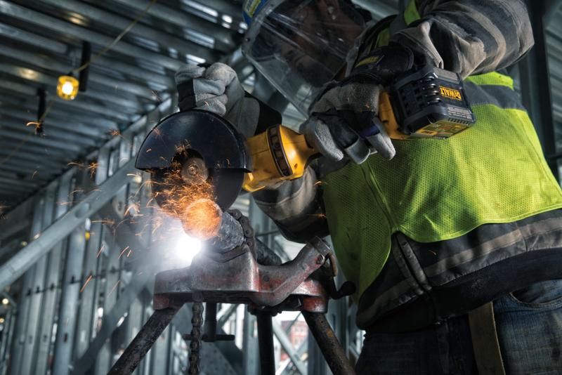 Person wearing safety gear using a DEWALT cordless angle grinder, producing sparks while cutting metal at a construction site.